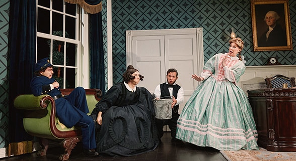 Four performers in period costumes gather in a Victorian-style room, including a seated figure in a blue uniform, a figure in a black dress near center stage, a figure holding a metal bucket, and a figure in a mint-green gown. The set includes patterned wallpaper, a tall window, a desk, and a framed portrait from Oh, Mary!.
