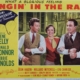 Color lobby card for Singin’ in the Rain featuring three performers linked arm in arm in the center of the image. The design includes a yellow background, a blue umbrella graphic with the words “MGM’s Technicolor Musical Treasure!,” and prominent red title text reading “Singin’ in the Rain.” Cast and production credits appear along the sides and bottom of the promotional artwork.