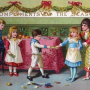 Victorian Christmas card showing four children gathered around a decorated table beneath a banner reading “Compliments of the Season.” Two children pull a Christmas cracker while another sits on a chair and a fourth stands nearby. Broken cracker contents and toys are scattered on the floor, with greenery garlands and red bows decorating the room.