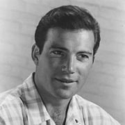 Black-and-white head-and-shoulders portrait of a person wearing a light plaid shirt, looking slightly off camera against a plain background.